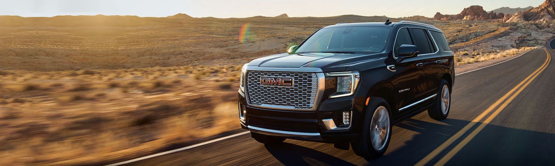 GMC Yukon Denali SUV driving on a highway at sunset.