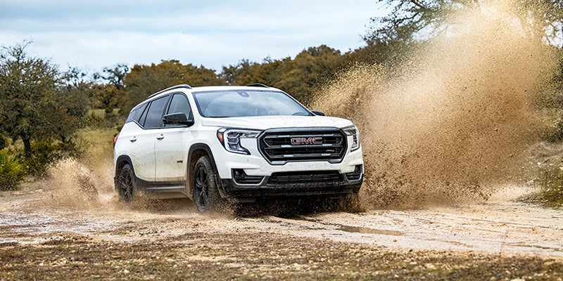 White 2024 GMC Terrain AT4 driving through a dirt path with dust clouds.